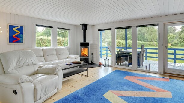 Un salón moderno con un sofá de cuero blanco, una mesa de centro y una chimenea. Hay ventanas amplias y vistas al exterior.