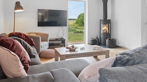 A modern living room with a sofa, a coffee table, a TV, and a wood-burning stove. - "Bjarka" - 700m from the sea by Interhome (Væggerløse)