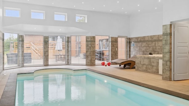 A modern indoor swimming pool with clear glass walls, a lounge area with a sunbed, and a view of the outside patio. - "Bjarka" - 700m from the sea by Interhome (Væggerløse)