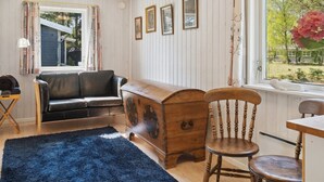 Una habitación acogedora con un cofre de madera, un sofá de cuero negro, una silla de madera y una ventana con vistas a zonas verdes.