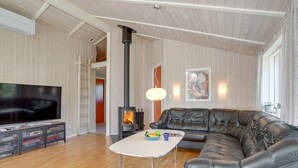 A modern living room with a large flat-screen TV, a leather sofa, a white coffee table, and a wood-burning stove.