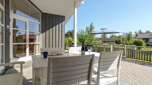 A covered patio with a table and chairs, a bottle of wine, and a book on the table.
