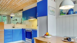 A modern kitchen with blue cabinets, a white refrigerator, and a wooden dining table with a bowl of fruit.