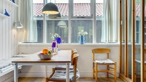A dining area with a table, chairs, a bowl of fruit, and a window with curtains.