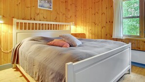 A wooden-paneled room with a bed, a window with curtains, and a picture on the wall.