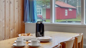 Una mesa de madera para comer con una cafetera, tazas y un bol de pasteles.