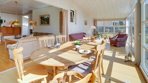 A spacious living area with a round wooden dining table, multiple chairs, a sofa, and a kitchen in the background. - "Sanna" - 330m from the sea by Interhome (Væggerløse)