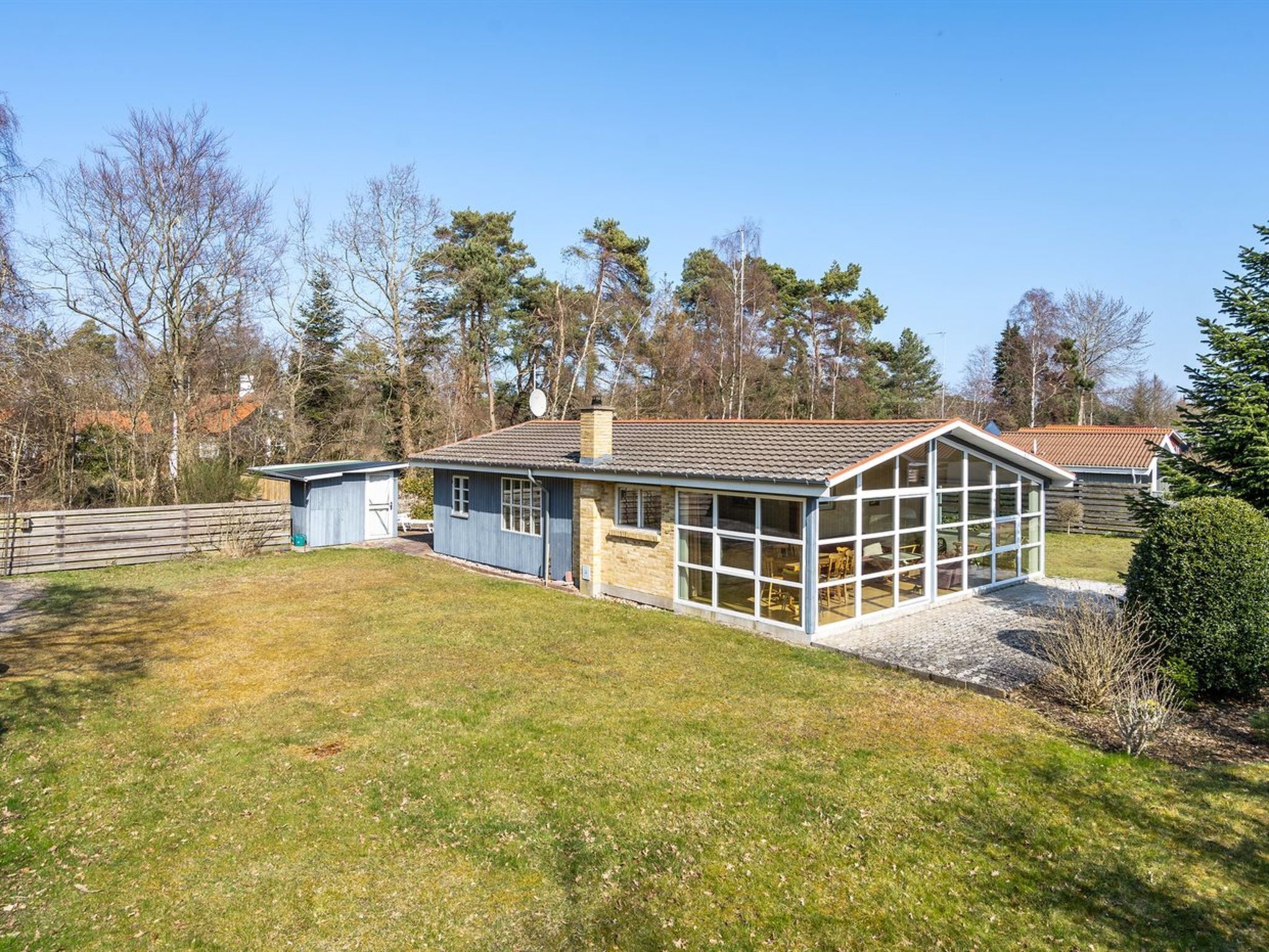 Een woning met een grote glazen conservatorium, een garage en een omheind erf.