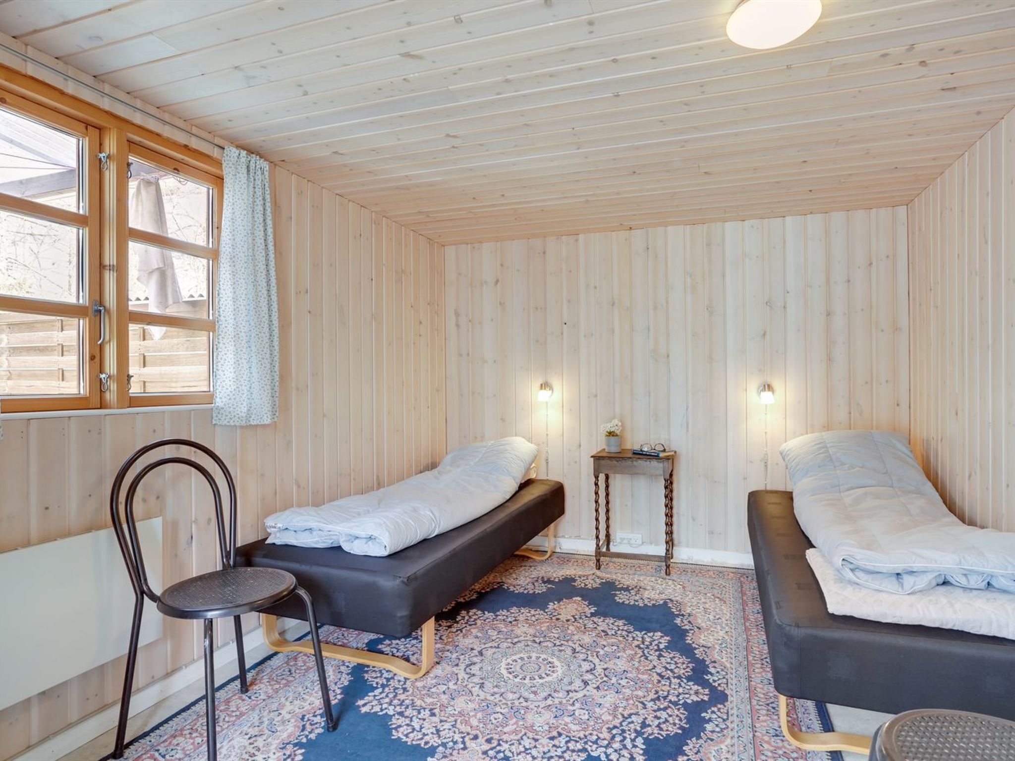 Ein gemütliches Zimmer mit zwei Betten, einem Sessel, einem kleinen Tisch und einem Fenster mit Vorhängen.