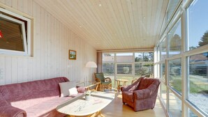 A spacious room with a wooden ceiling, large windows, a pink sofa, a wooden coffee table, and a wicker chair. - "Sanna" - 330m from the sea by Interhome (Væggerløse)