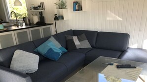 A modern living room with a dark grey sectional sofa, a glass coffee table, and a kitchen area in the background.