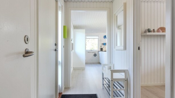 A hallway with white walls, a black doormat, and a white door with a keyhole.