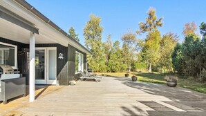 A modern house with a covered patio, a barbecue grill, and a lounge chair.