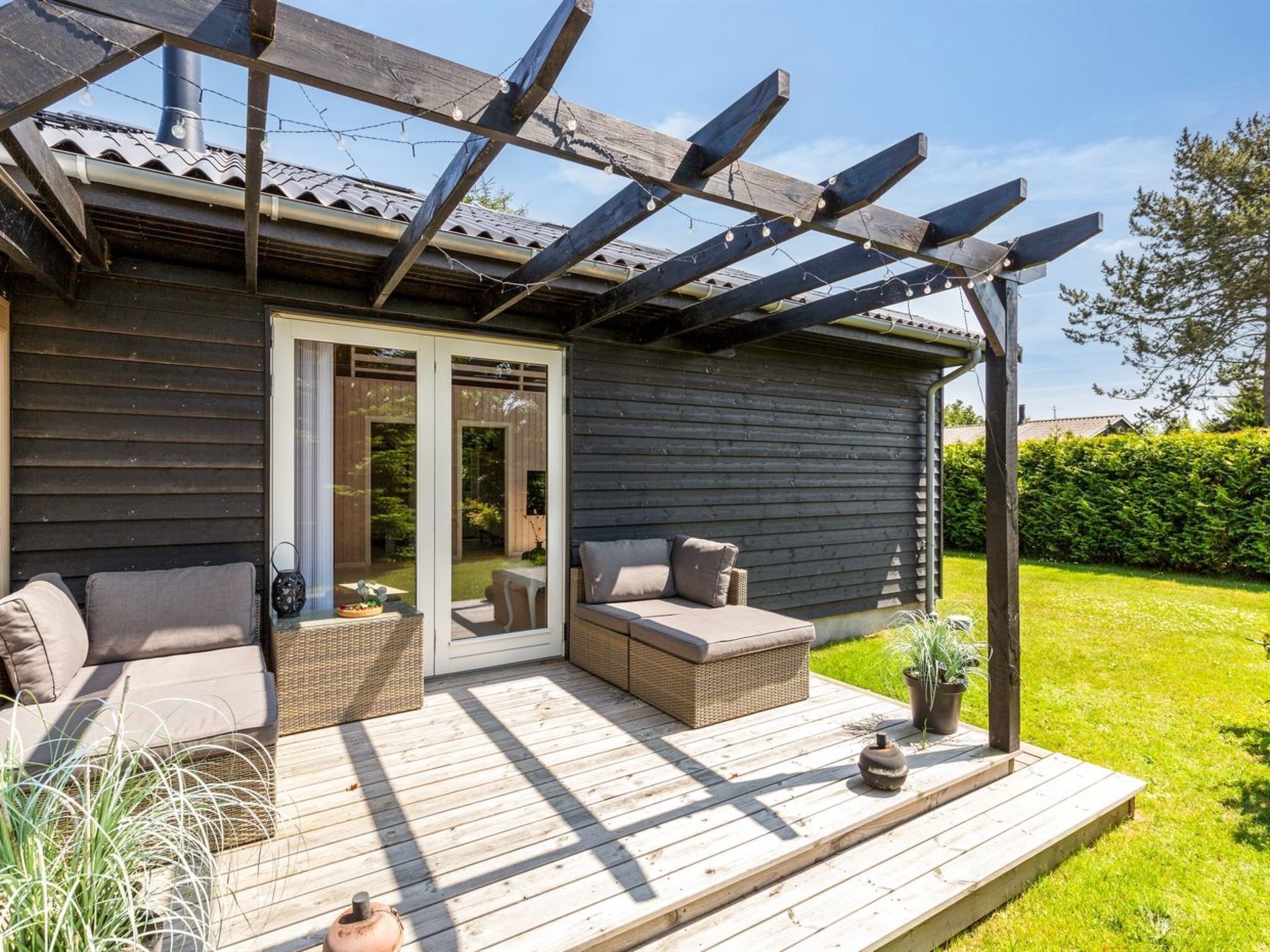 Eine Holzterrasse mit Gartenmöbeln, einer Pergola und Blick auf einen Garten.