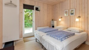 Une chambre avec des murs en bois, un lit avec une literie blanche, une table de chevet, une étagère et une fenêtre donnant sur un paysage verdoyant.
