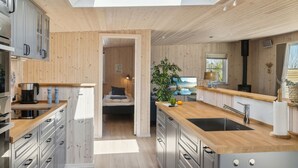 A modern kitchen with wooden cabinetry, a central island with a sink, and a dining area with a table and chairs. - "Engli" - 90m from the sea by Interhome (Væggerløse)