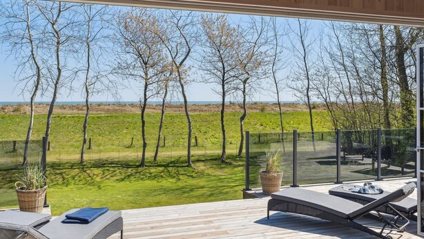 A deck with two lounge chairs and a small table, overlooking a grassy field and trees. - "Engli" - 90m from the sea by Interhome (Væggerløse)