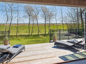 Eine Terrasse mit zwei Liegestühlen und einem kleinen Tisch, mit Blick auf ein Wiesfeld und Bäume.