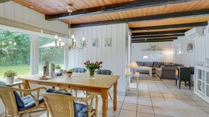 Una cocina amplia con zona de comedor, con una mesa de madera, sillas de mimbre y vistas al jardín a través de grandes ventanales.