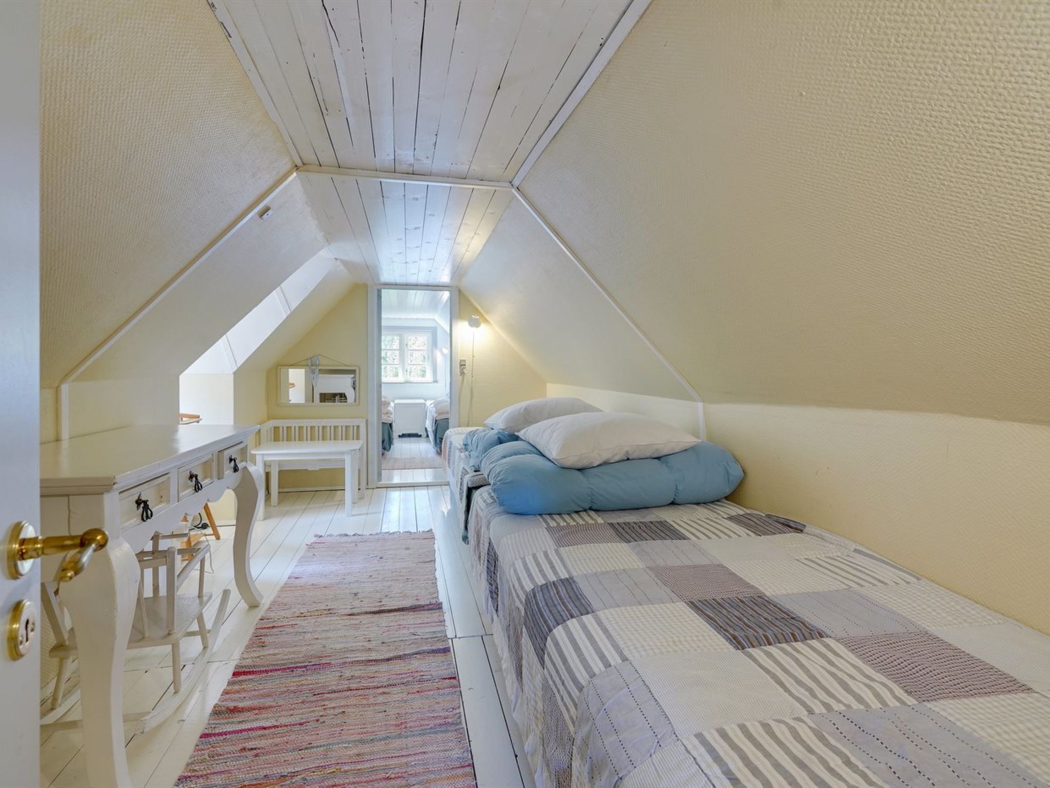 Un pequeño y acogedor dormitorio en el ático con una cama, un banco y un aparador.