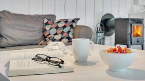 Una sala de estar acogedora con un sofá, una taza blanca, un cuenco de bocadillos y un libro con gafas sobre una mesa.