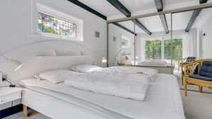 Un dormitorio moderno con una cama grande, una mesita de noche, una lámpara y una ventana con vistas a zonas verdes.