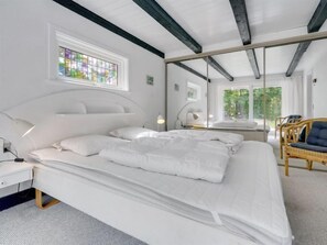 Relax in a serene space with a large bed, a spacious mirror, and a chair with a cushion.