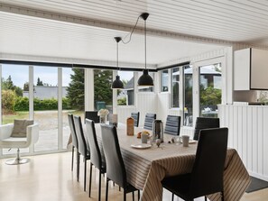A modern dining area with a long table, black chairs, and pendant lighting.