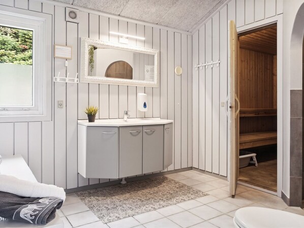 A bathroom with a white vanity, a mirror, a towel rack, and a wooden door leading to a shower area.