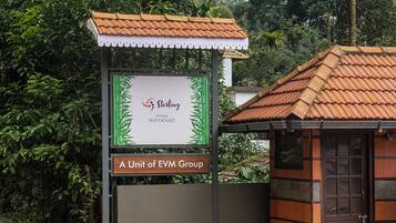 Señal de Sterling Vythiri Wayanad, una división de EVM Group, con un techo de tejas tradicionales y una pequeña estructura de madera cerca.