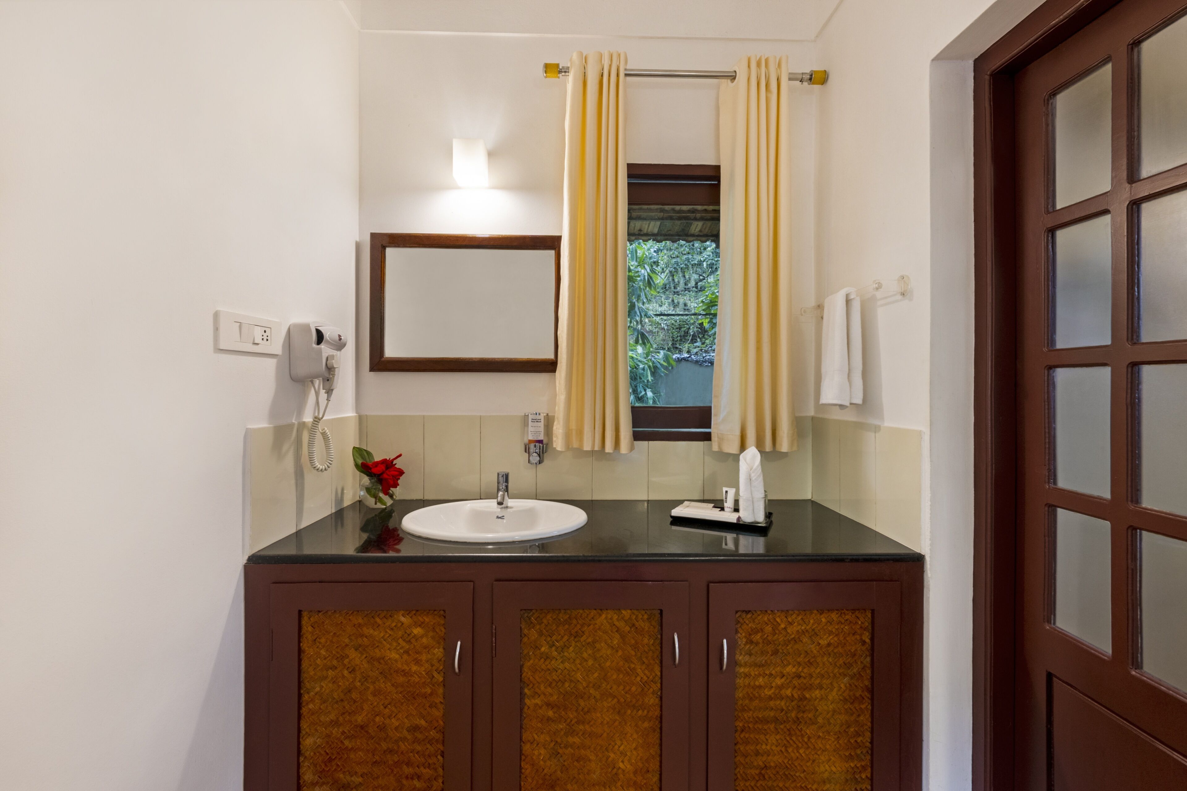 Baño con lavamanos, espejo y ventana. Hay un perchero y un teléfono.