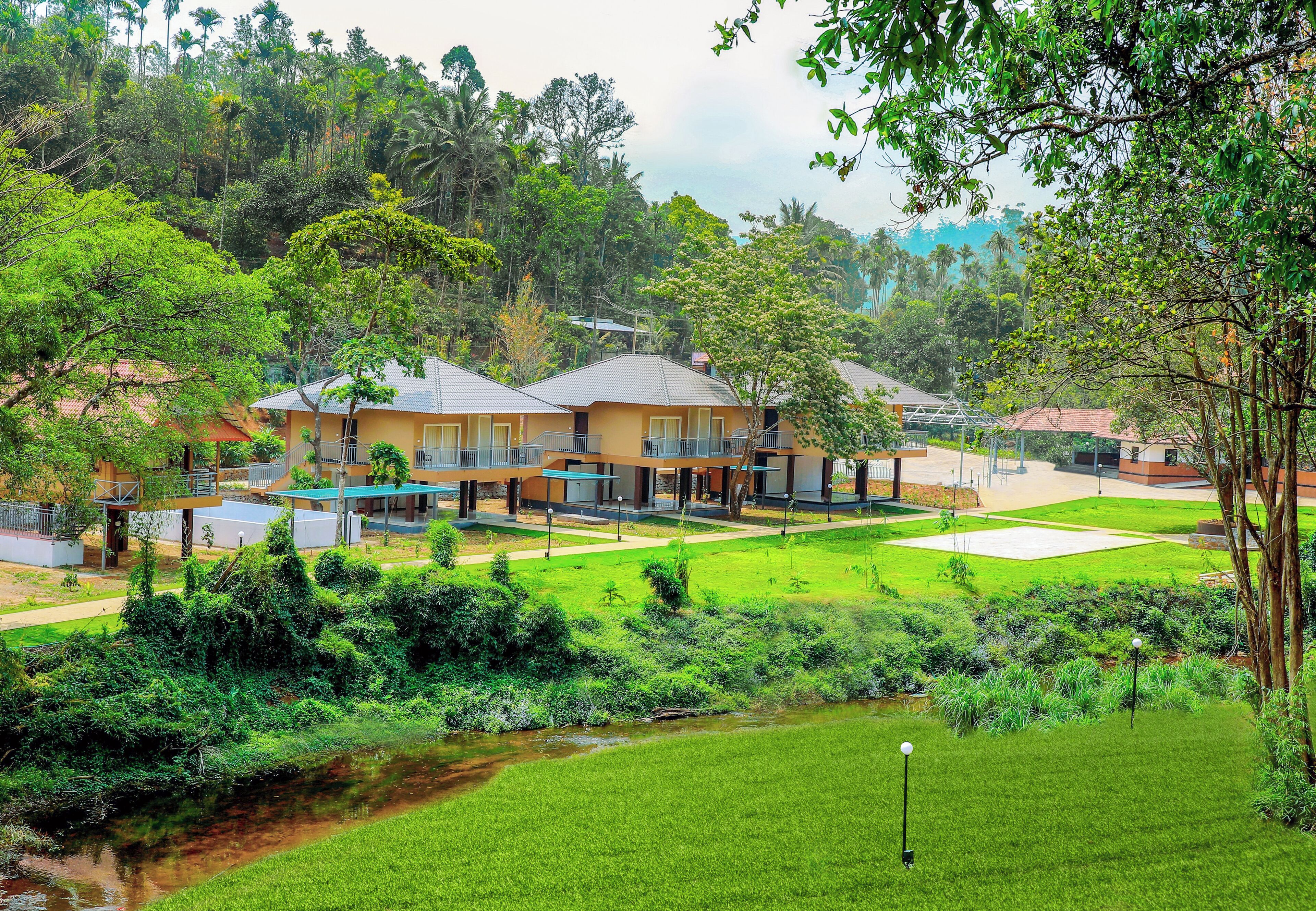 A residential area with multiple houses, a grassy lawn, and a small stream.
