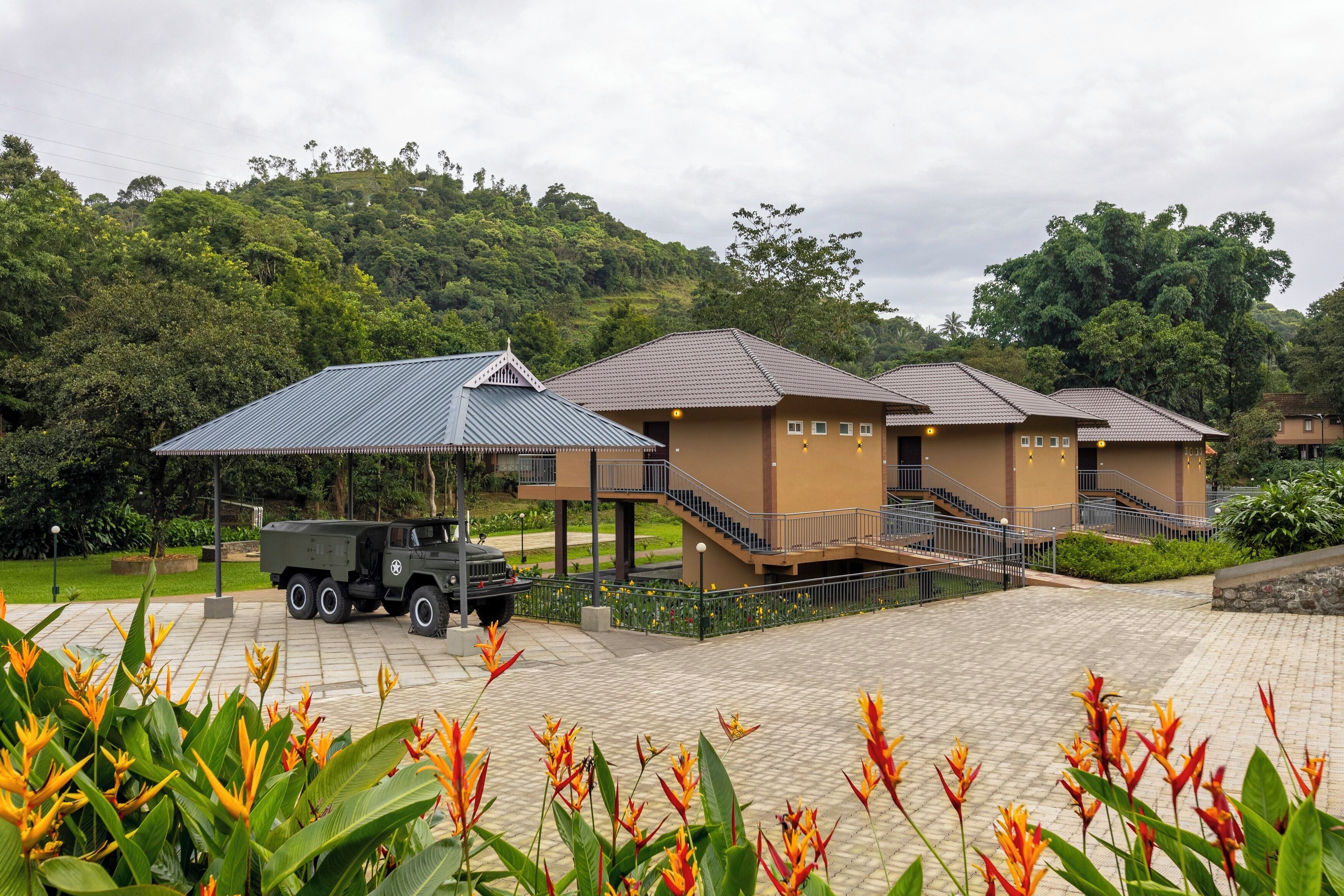 A hotel with a paved courtyard, a truck, and a lush green hillside in the background.