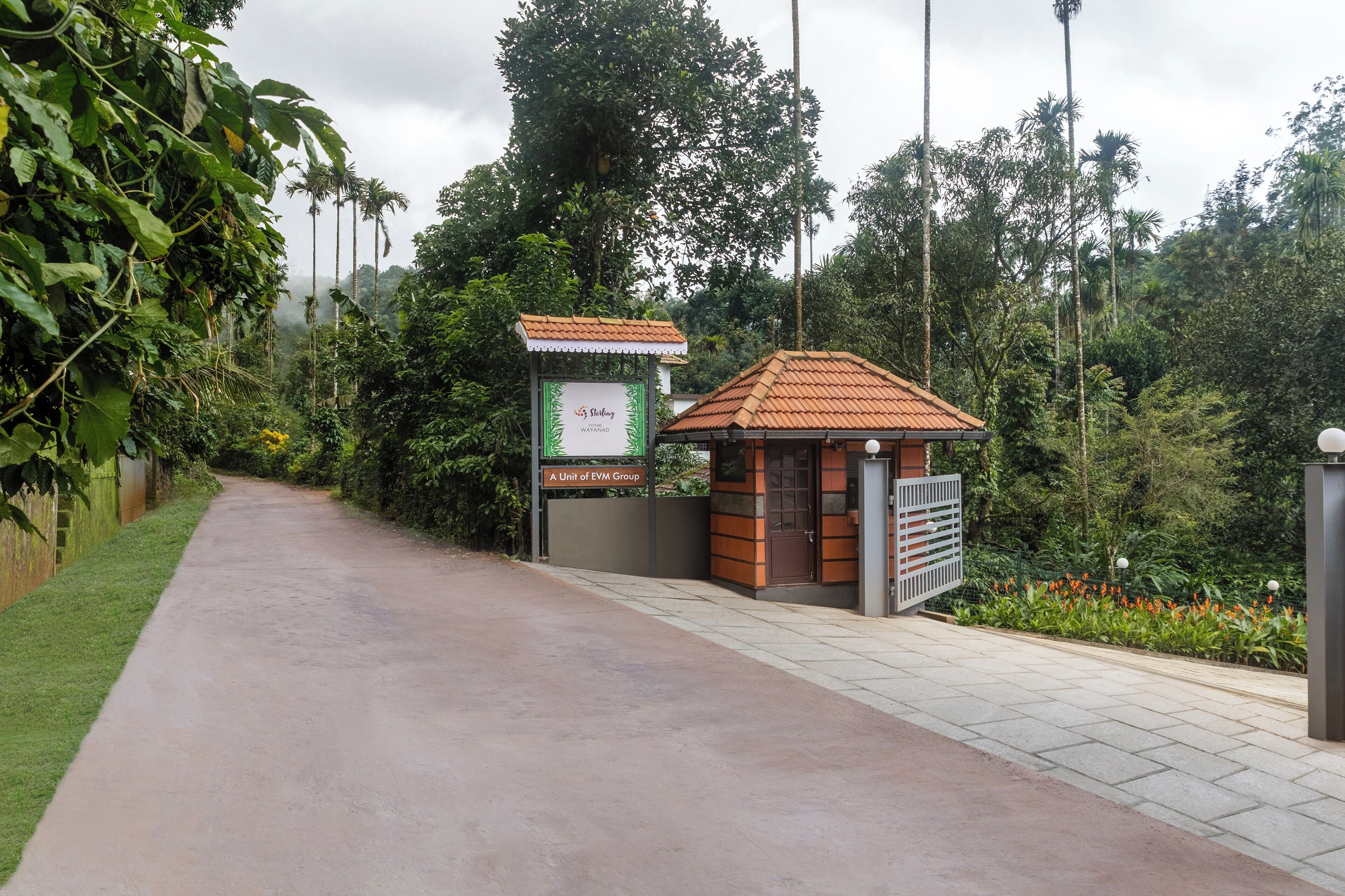 A pathway leading to a small building with a tiled roof, surrounded by lush greenery and tall trees.
