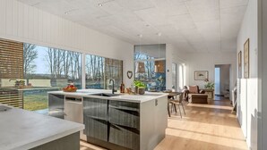 Une cuisine moderne dotée d’un grand îlot central, de planchers en bois et de grandes fenêtres offrant une vue sur l’extérieur.