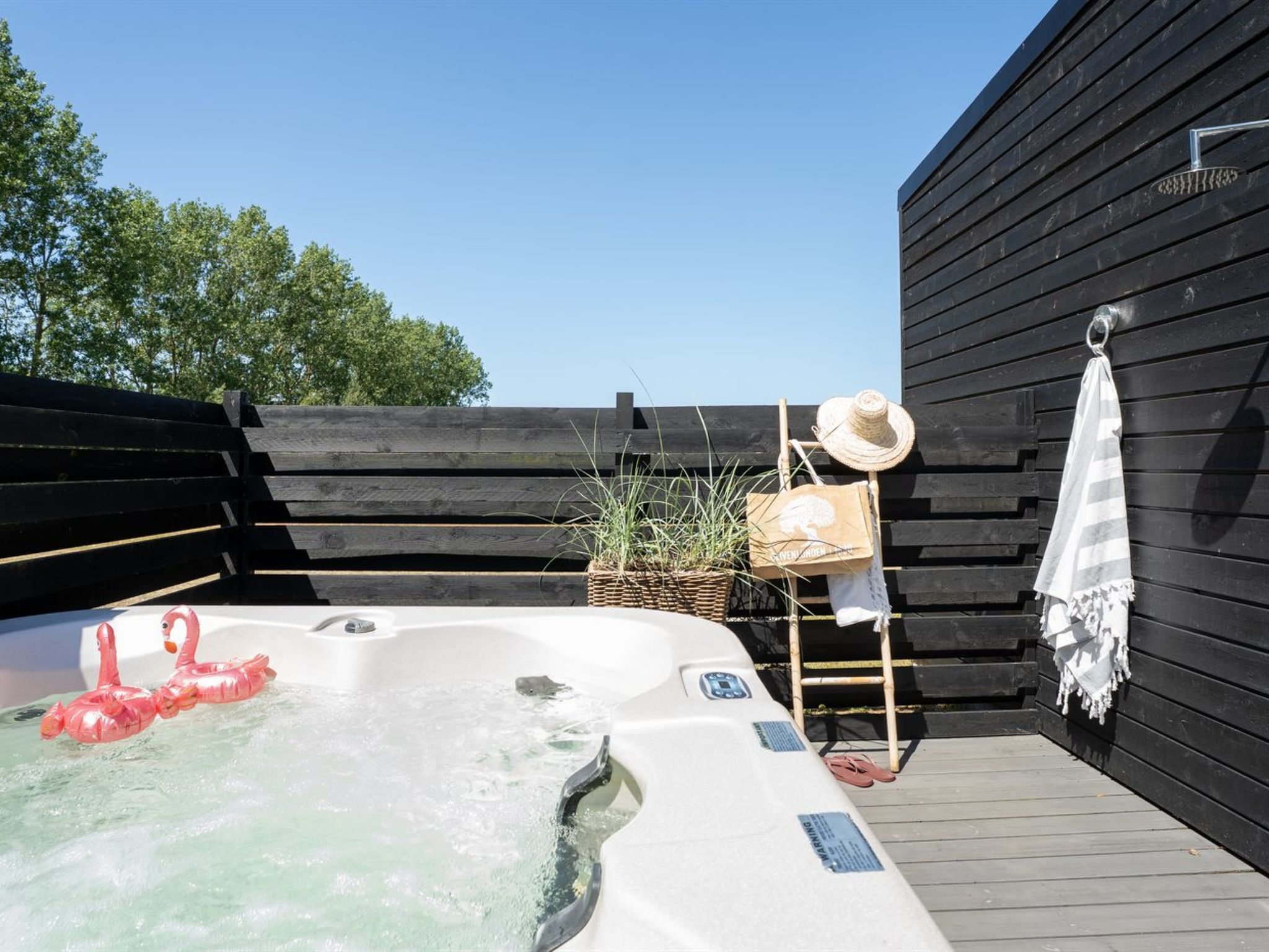 A hot tub with a wooden deck, a wooden fence, and a hat on a rack.