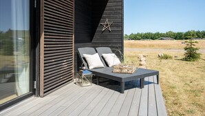 Un espace extérieur moderne, aménagé avec une terrasse en bois, deux fauteuils confortables dotés de coussins et une décoration en forme d’étoile sur le mur.
