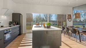 Une cuisine moderne dotée d’un îlot central, de grandes fenêtres et d’un coin repas offrant une vue agréable.