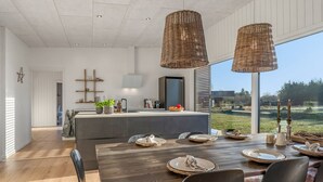 Une cuisine moderne dotée d’un grand îlot central, d’une table à manger en bois et de luminaires suspendus en osier.