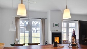 Eine moderne Küche mit Holzarbeitsplatte, hängenden Pendelleuchten, einem Kamin und großen Fenstern mit Vorhängen.