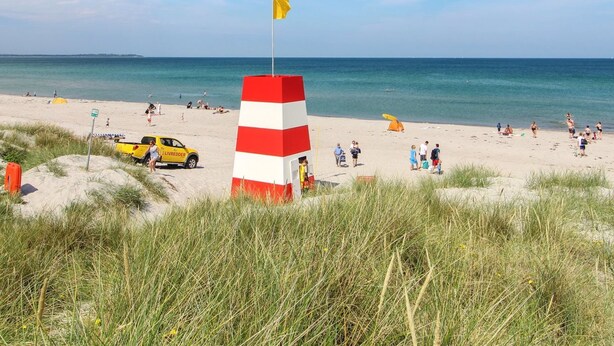 Ein Strand mit einem roten und weißen Leuchtturm, blauem Himmel und ruhiger See.
