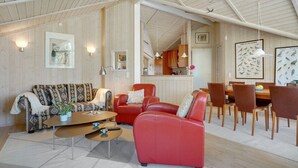 Ein großzügiger Wohnbereich mit hoher Decke, Holzwänden, einem roten Ledersofa, einem gemusterten Sofa, einem Couchtisch und einem Essbereich mit Holzsesseln.
