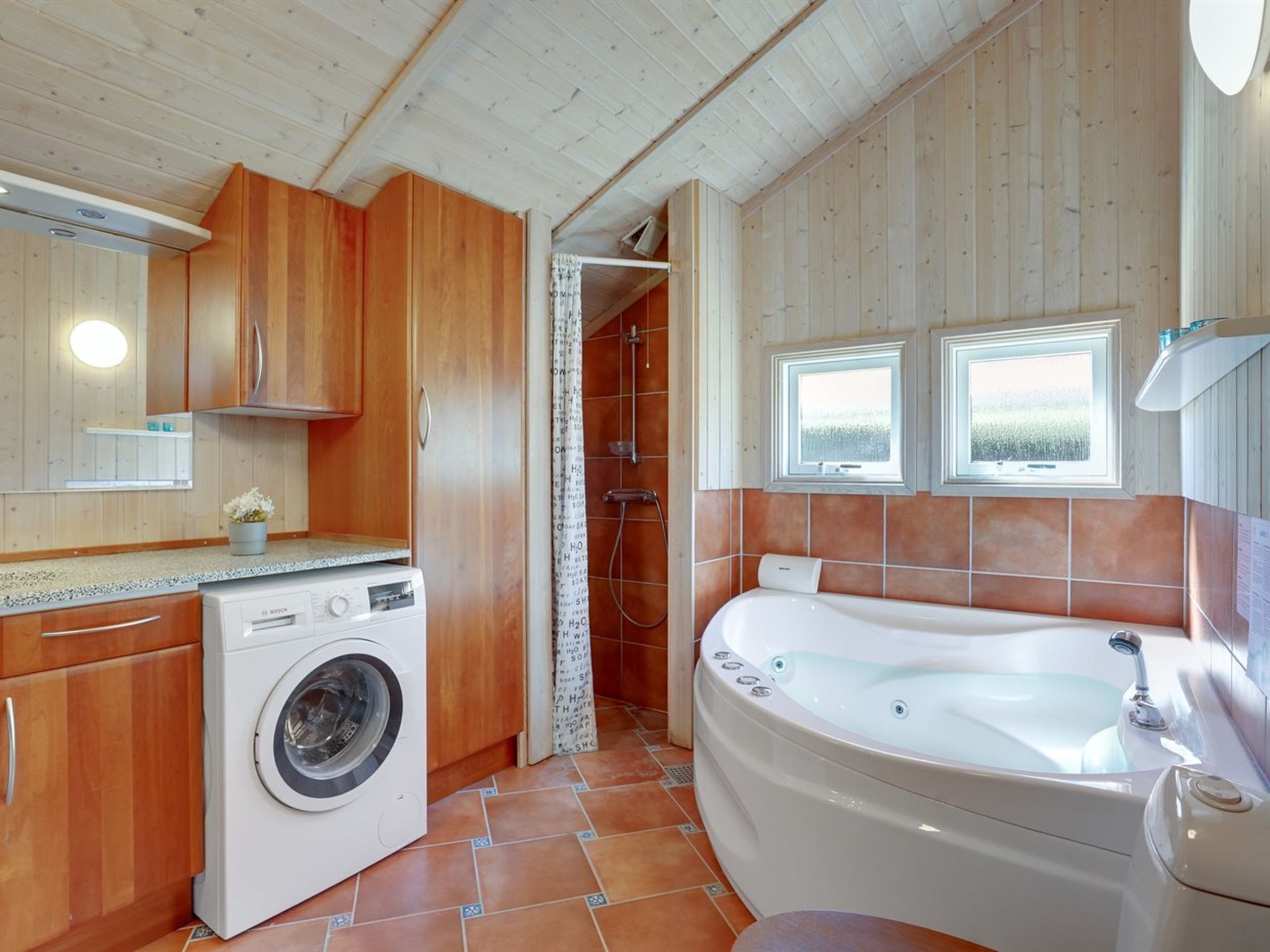A compact kitchen with a washing machine, wooden cabinets, and a large bathtub.