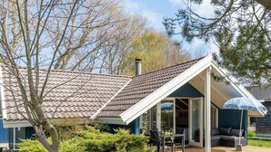 Une maison avec un toit en tuiles, un patio couvert avec des meubles d’extérieur et un jardin.