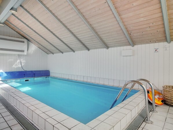 Ein Innenpool mit gefliestem Rand, einem blauen Poolbereich und einer überdachten Dachkonstruktion.