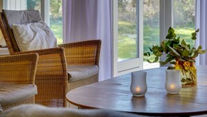 A room with wicker furniture, a round table, and a view of greenery outside.