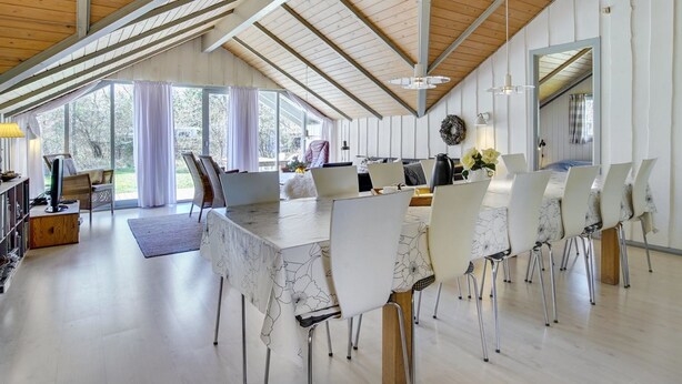 A spacious dining area with a long table, white chairs, and a high ceiling with wooden beams.