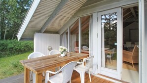 An outdoor deck with a wooden table and white plastic chairs, a glass door leading to an indoor area with a wicker sofa.
