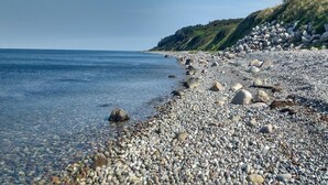 A pebbled beach with clear water, a rocky shoreline, and a forested hill in the background. - "Miona" - 725m from the sea by Interhome (Kalundborg)