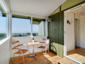 A balcony with wooden flooring, two metal chairs, a small table, and a potted plant.